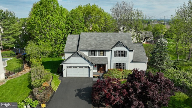view of front facade with roof with shingles, an attached garage, a front lawn, and driveway