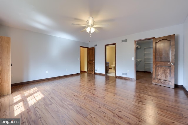 unfurnished bedroom featuring a spacious closet, baseboards, visible vents, and wood finished floors