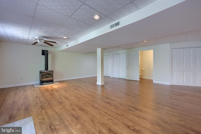 basement with a wood stove, wood finished floors, and baseboards