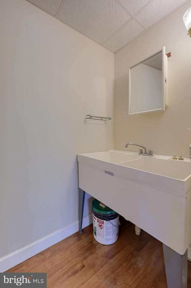 bathroom featuring baseboards, an ornate ceiling, a sink, and wood finished floors