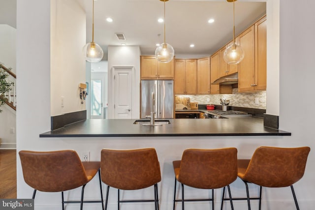 kitchen featuring a breakfast bar area, stainless steel refrigerator, decorative light fixtures, kitchen peninsula, and light brown cabinets