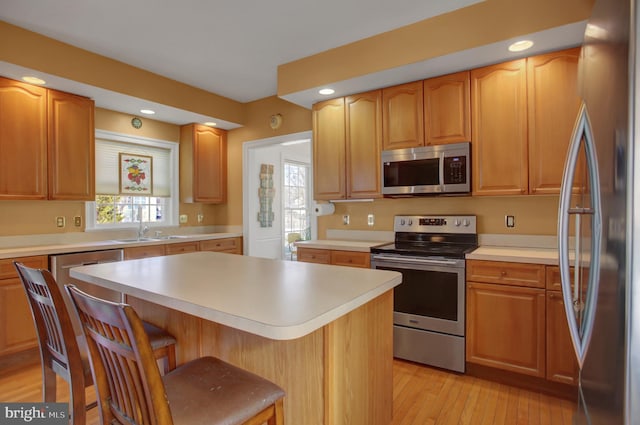 kitchen with sink, a breakfast bar, stainless steel appliances, a center island, and light hardwood / wood-style floors