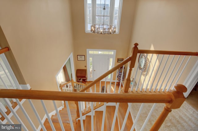 staircase with a high ceiling, plenty of natural light, hardwood / wood-style floors, and a notable chandelier