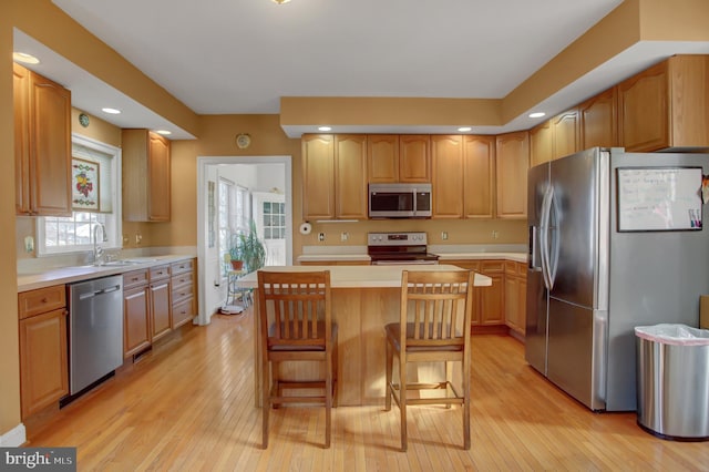 kitchen with a kitchen island, appliances with stainless steel finishes, a kitchen breakfast bar, and light hardwood / wood-style floors