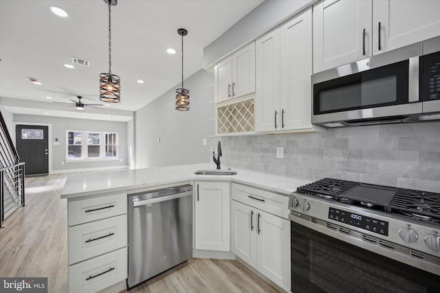 kitchen featuring pendant lighting, sink, stainless steel appliances, light hardwood / wood-style floors, and white cabinets