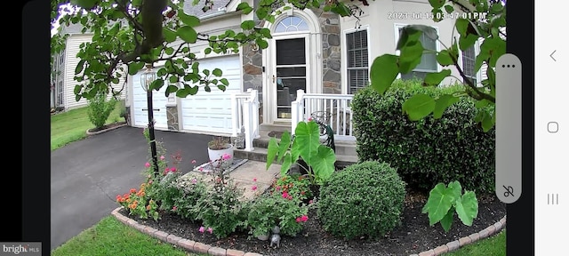 property entrance featuring a garage, stone siding, and aphalt driveway