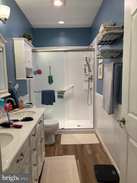 bathroom featuring wood-type flooring, toilet, a shower with shower door, and vanity