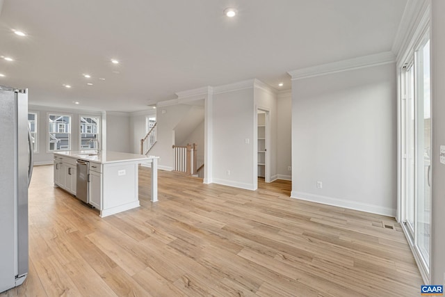 kitchen with a breakfast bar, crown molding, light hardwood / wood-style flooring, stainless steel appliances, and a kitchen island with sink