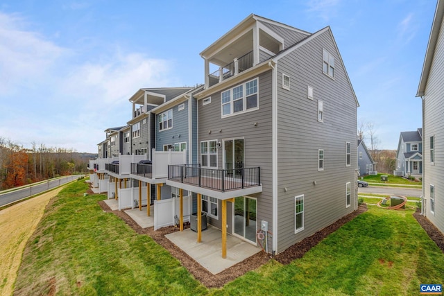 rear view of house featuring a balcony, a patio area, and a lawn