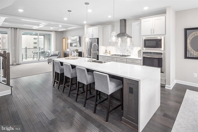 kitchen featuring wall chimney exhaust hood, sink, decorative light fixtures, stainless steel appliances, and white cabinets