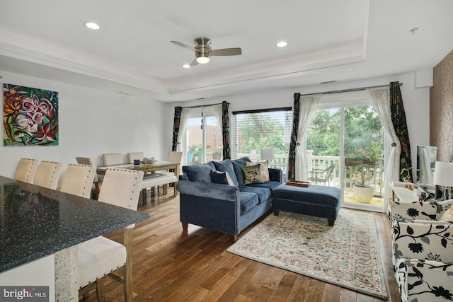 living room featuring ceiling fan, wood-type flooring, and a tray ceiling