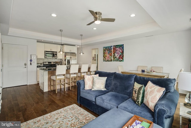 living room with ceiling fan, dark hardwood / wood-style flooring, and a tray ceiling