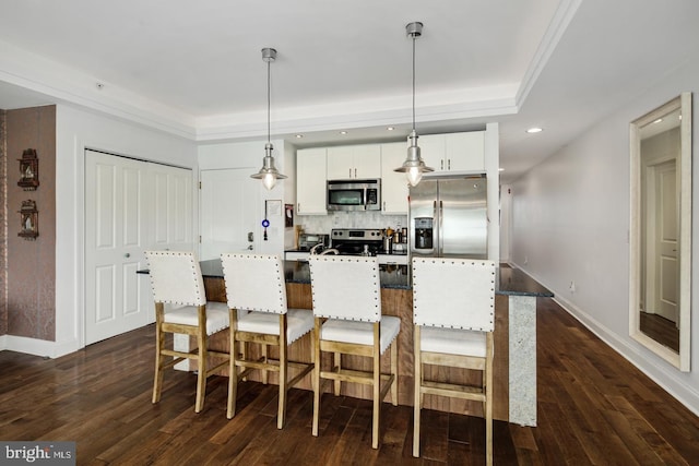 kitchen with appliances with stainless steel finishes, pendant lighting, white cabinets, and a tray ceiling