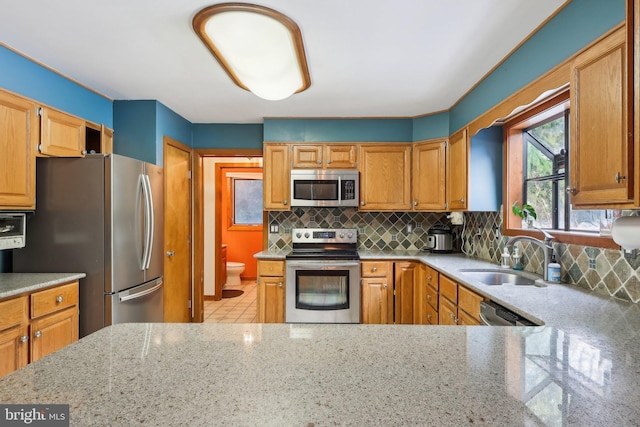 kitchen featuring sink, backsplash, stainless steel appliances, light stone countertops, and kitchen peninsula