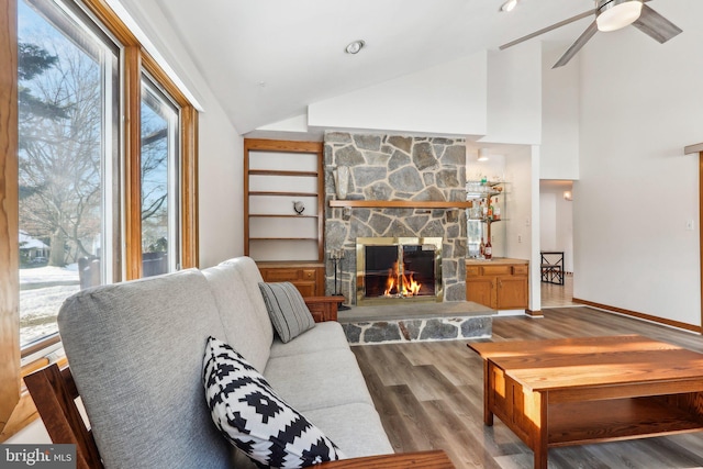 living room featuring a stone fireplace, plenty of natural light, lofted ceiling, and light wood-type flooring