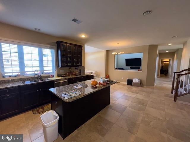 kitchen featuring sink, light stone counters, decorative light fixtures, a chandelier, and a kitchen island