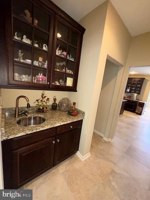 bar featuring dark brown cabinetry, sink, and light stone counters