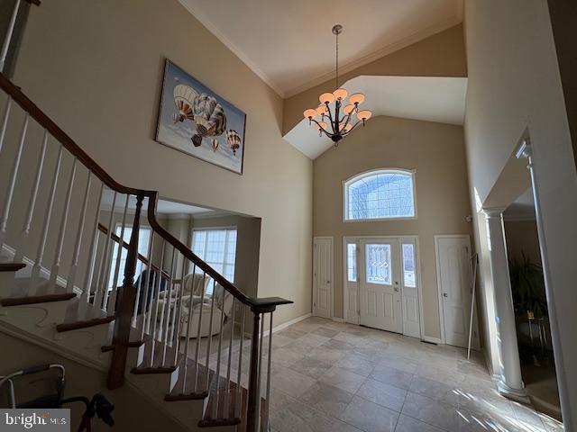 foyer with a towering ceiling, a chandelier, and decorative columns