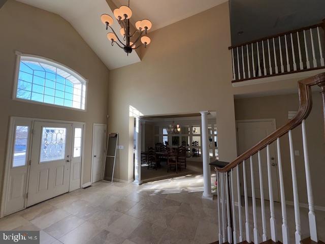 foyer with ornate columns, a notable chandelier, and high vaulted ceiling