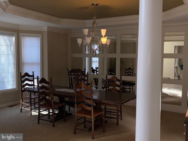 carpeted dining area with decorative columns, a notable chandelier, and a tray ceiling