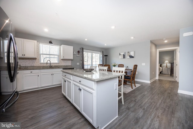 kitchen featuring white cabinets, dark hardwood / wood-style flooring, stainless steel fridge, a kitchen bar, and a center island