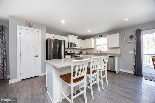 kitchen featuring a breakfast bar area, white cabinetry, appliances with stainless steel finishes, a kitchen island, and backsplash