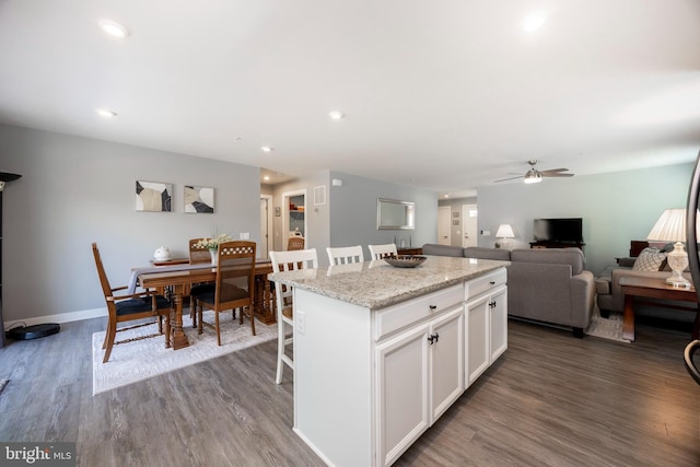 kitchen featuring dark hardwood / wood-style floors, a breakfast bar, white cabinets, a center island, and light stone counters