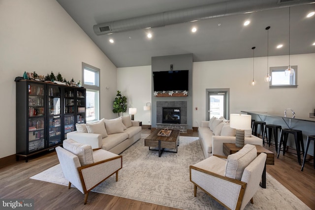 living room with a tile fireplace, high vaulted ceiling, and light hardwood / wood-style flooring