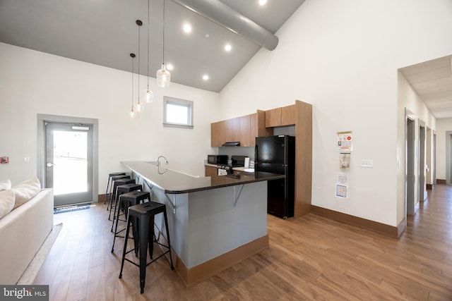 kitchen with a kitchen bar, high vaulted ceiling, light hardwood / wood-style flooring, black refrigerator, and pendant lighting