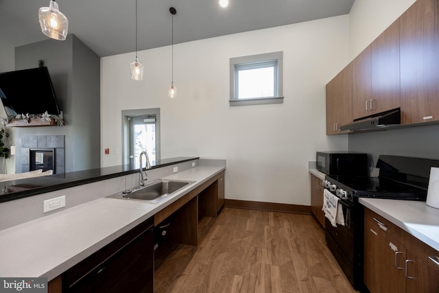 kitchen featuring sink, decorative light fixtures, a fireplace, light hardwood / wood-style floors, and black appliances