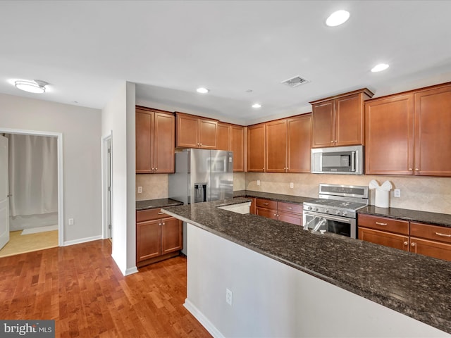 kitchen with dark stone countertops, backsplash, light hardwood / wood-style floors, and appliances with stainless steel finishes