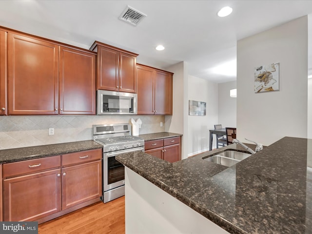 kitchen featuring appliances with stainless steel finishes, sink, dark stone countertops, decorative backsplash, and light hardwood / wood-style flooring