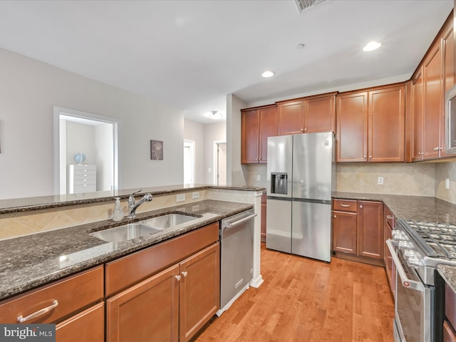 kitchen featuring sink, appliances with stainless steel finishes, decorative backsplash, dark stone counters, and light wood-type flooring