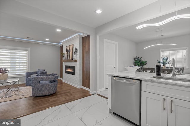 kitchen featuring sink, dishwasher, light stone counters, a fireplace, and white cabinets