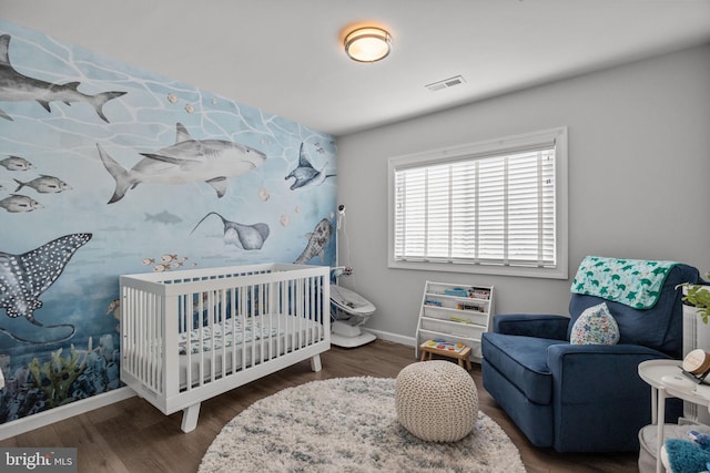 bedroom with dark wood-type flooring and a crib