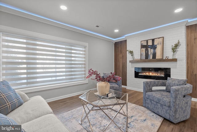 living room with hardwood / wood-style flooring, crown molding, and a large fireplace