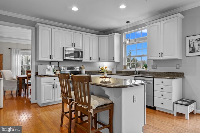 kitchen with white cabinetry, stainless steel appliances, decorative light fixtures, and a kitchen island