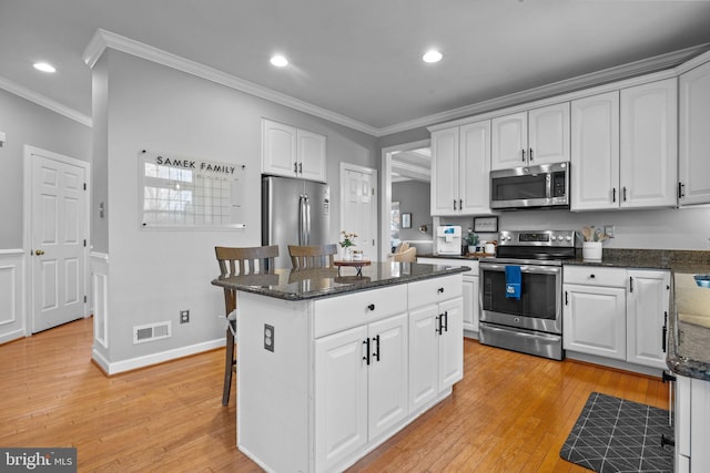 kitchen with white cabinetry, ornamental molding, stainless steel appliances, and a breakfast bar area