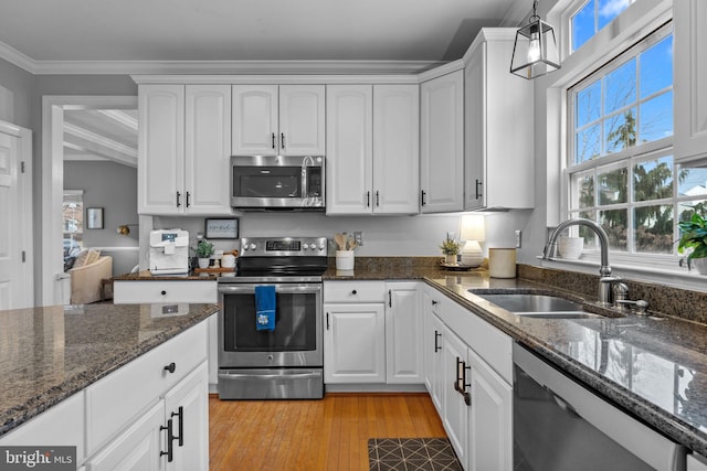 kitchen featuring white cabinetry, stainless steel appliances, decorative light fixtures, and dark stone counters