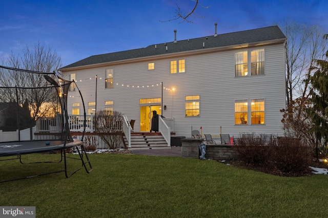 back house at dusk featuring a wooden deck, a trampoline, and a lawn