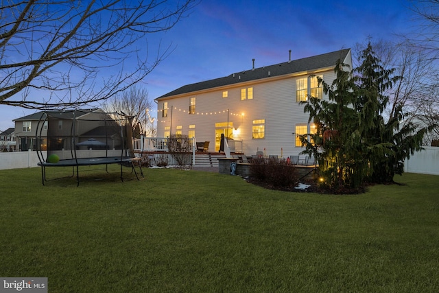 back house at dusk featuring a deck, a trampoline, and a lawn