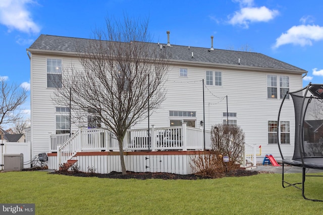 rear view of house with a trampoline, a wooden deck, and a yard