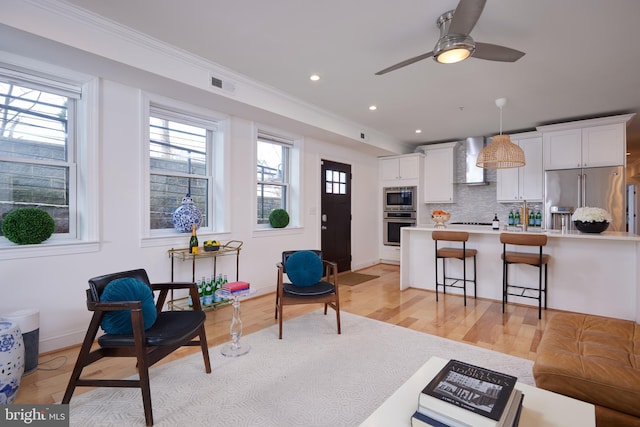 living room with crown molding, ceiling fan, and light hardwood / wood-style floors