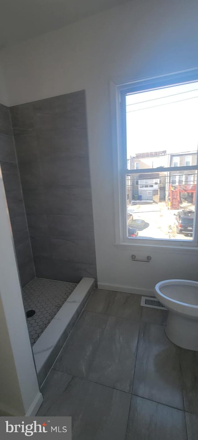 bathroom featuring toilet, tile patterned flooring, and a tile shower