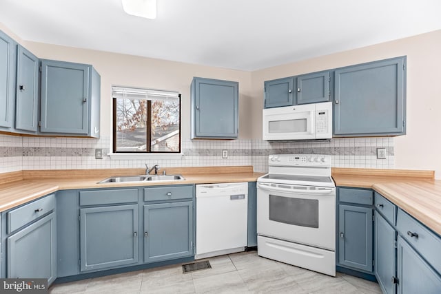 kitchen featuring white appliances, blue cabinets, sink, and light tile patterned floors