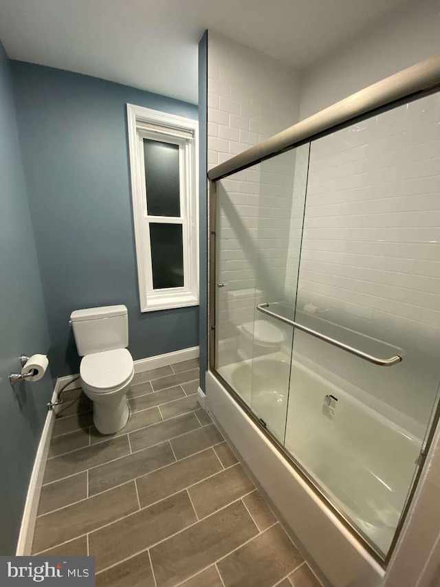 bathroom with bath / shower combo with glass door and toilet