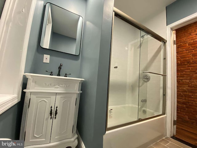 bathroom with brick wall, combined bath / shower with glass door, and vanity