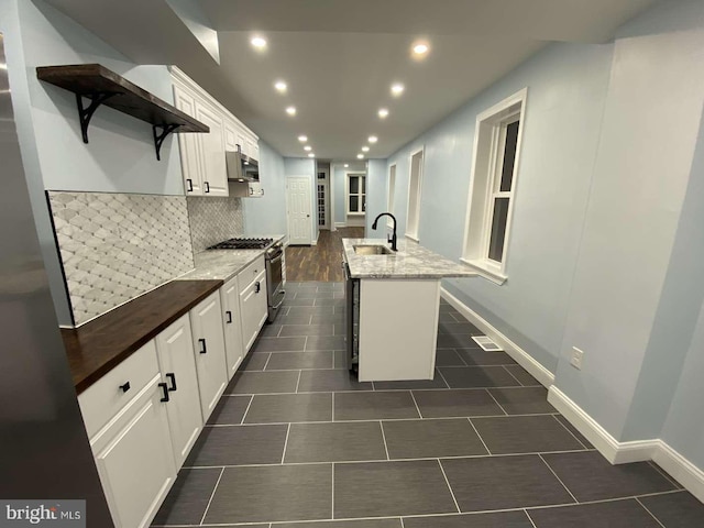 kitchen with sink, light stone counters, a center island with sink, stainless steel range with gas cooktop, and white cabinets