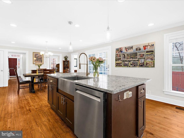 kitchen featuring wood-type flooring, decorative light fixtures, dishwasher, an island with sink, and light stone countertops