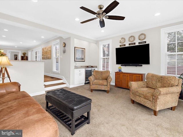 living room featuring beverage cooler, ornamental molding, bar, ceiling fan, and light carpet